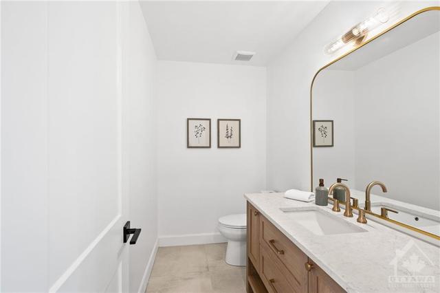 The main floor powder room was designed to be a statement bath. Custom white oak cabinetry, Silestone quartz, champagne bronze Delta faucet, oversized mirror and beautiful floor tile. (Tiled floor | Image 12