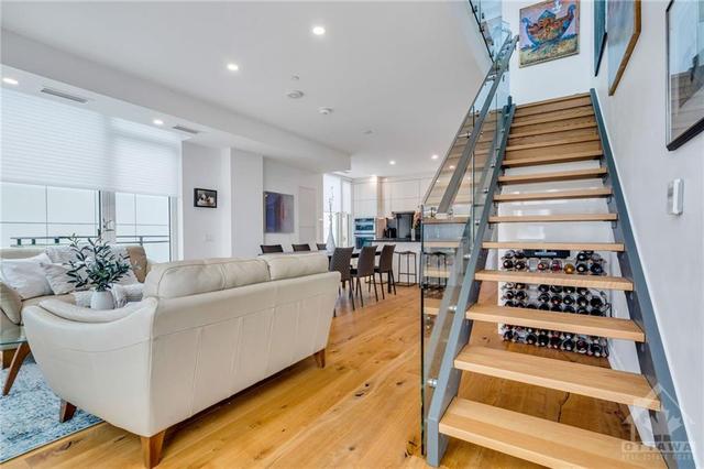Signature open-riser wood staircase with glass guards leads to 2nd level | Image 16