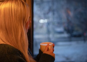 Woman staring out of a window with a mug in the cold weather.