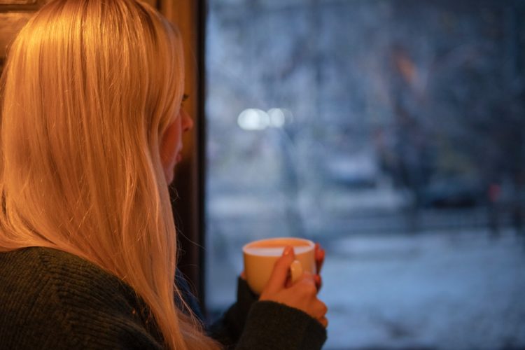 Woman staring out of a window with a mug in the cold weather.