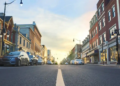 A city street lined with parked cars on both sides, showcasing urban life and traffic patterns.