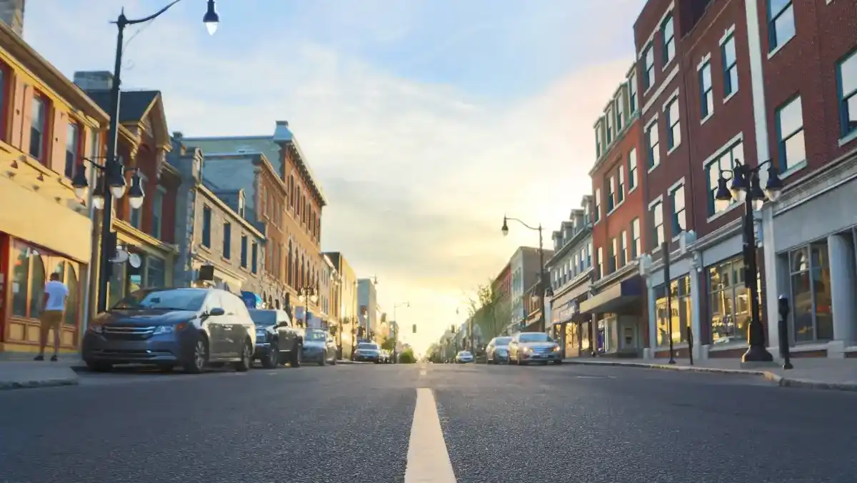 A city street lined with parked cars on both sides, showcasing urban life and traffic patterns.