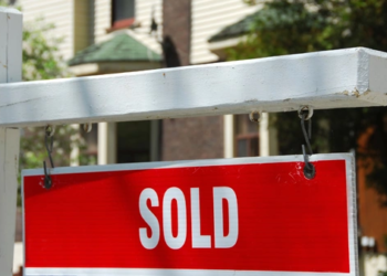 A white picket cross with a hanging sign that says "SOLD" in red.