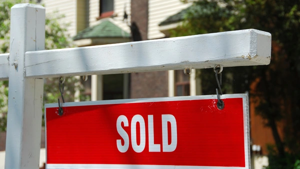 A white picket cross with a hanging sign that says "SOLD" in red.