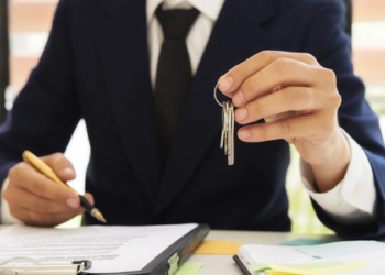 A person in a suit has a set of keys in one hand and a pen in the other.