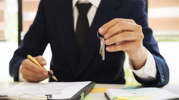 A person in a suit has a set of keys in one hand and a pen in the other.