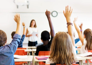 A group of children with their hands raised in a classroom.