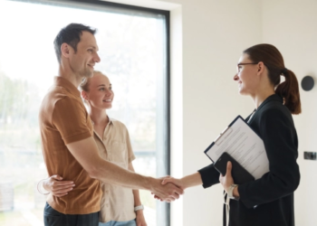 A couple shakes hands with a real estate agent.