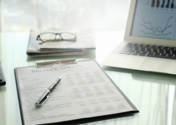 A clipboard with a balance sheet on it and a laptop and calculator.