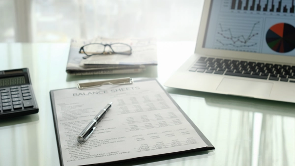 A clipboard with a balance sheet on it and a laptop and calculator.