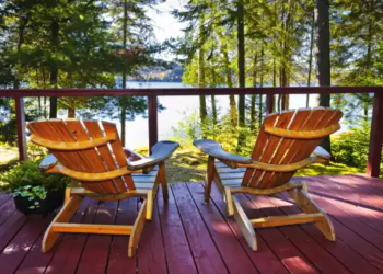 Two Muskoka chairs on a patio overlooking a lake.