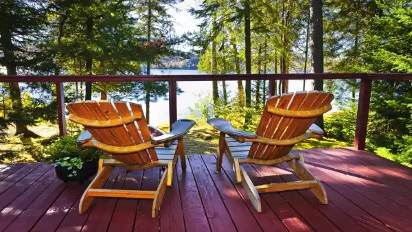 Two Muskoka chairs on a patio overlooking a lake.