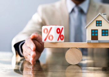 A wooden house and dice with a percent sign balance on a wooden beam.