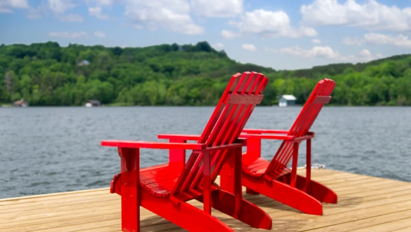 Two red Muskoka chairs on a dock.