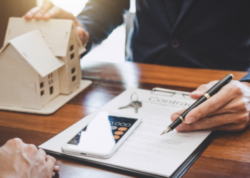 Someone presenting a contract and a small wooden house.