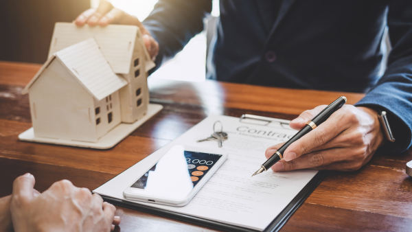 Someone presenting a contract and a small wooden house.