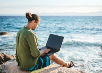 A man works on his laptop next to the ocean