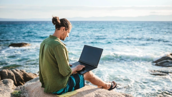 A man works on his laptop next to the ocean