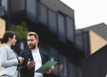 Two business people stand outside of a home.