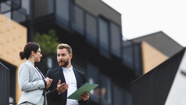Two business people stand outside of a home.
