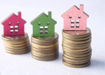 Small cardboard homes on top of stacked piles of coins