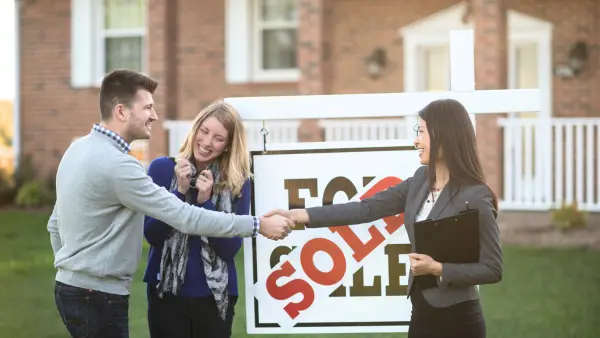 Young happy couple shaking hands with real estate agent