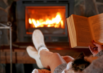 A person reading a book by their fireplace.
