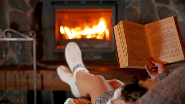 A person reading a book by their fireplace.