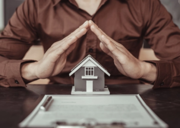 A real estate agent puts their hands over a tiny house on a table