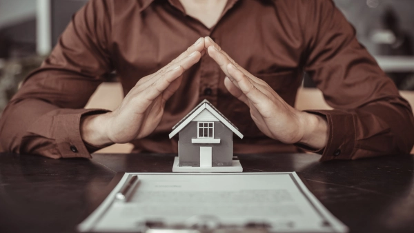 A real estate agent puts their hands over a tiny house on a table