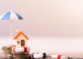 A tiny clay model house stacked up on some coins.