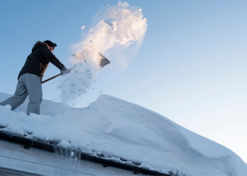 A man shoveling snow off of his roof