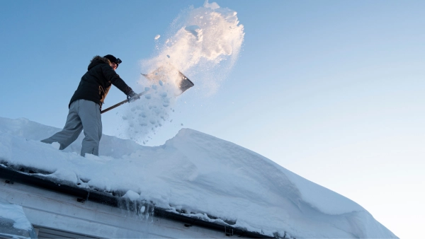 A man shoveling snow off of his roof