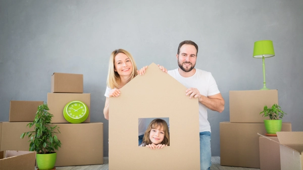A family poses with a cardboard box that is cut into the shape of a house