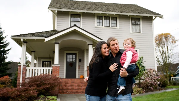 A family of three standing in front of a detached home.