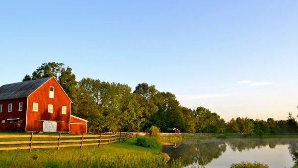 A red barn in the middle of a large field surrounded by a lake.