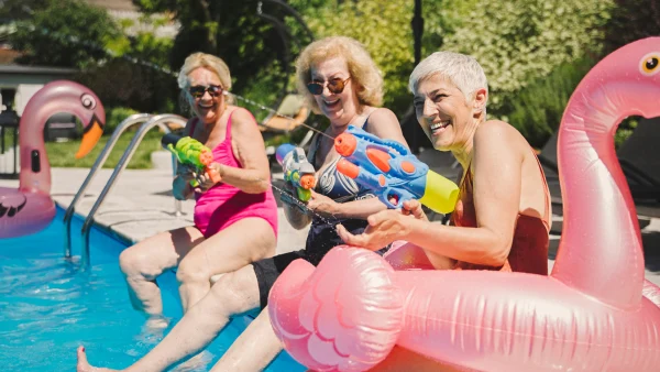 Three women play with water guns at a pool