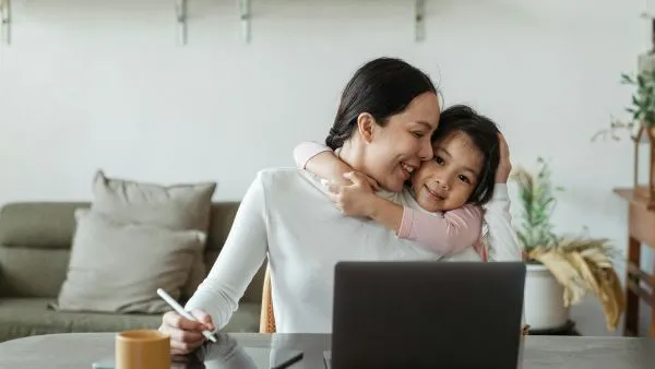Mom working on laptop child hugging her