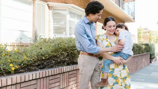 Parents holding young child outside apartment building