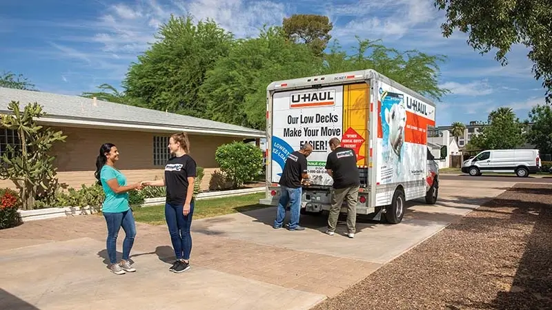 A customer shakes hands with a Moving Help Service Provider after completing a successful job of loading the customer’s belongings into a U-Haul truck rental. Two labor-only providers in the background close the U-Haul truck rental.