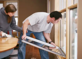 Two people sealing gaps and cracks around a window.