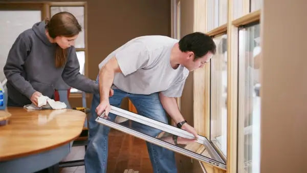Two people sealing gaps and cracks around a window.