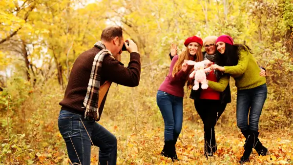 A family taking photos with fall leaves in the back.
