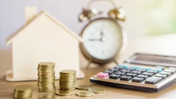 Coins, calculator, a clock and a small, wooden house.