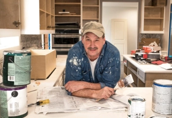 A person holding a paintbrush in the middle of a kitchen undergoing renovations.