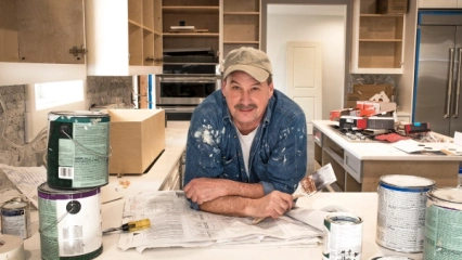 A person holding a paintbrush in the middle of a kitchen undergoing renovations.