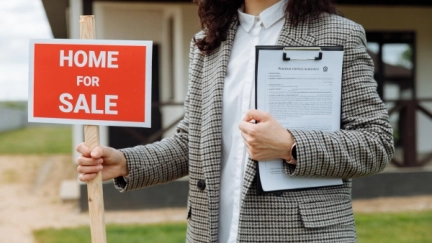 A person holding a clipboard and a home for sale sign.