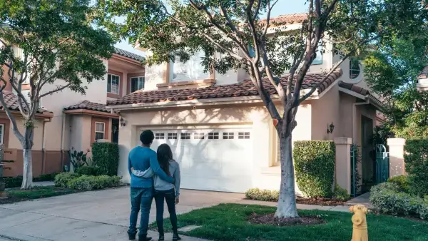 Two people stand outside of a home looking at it from the outside.