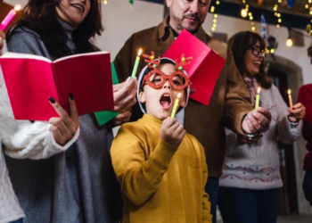 People singing and blowing out candles while wearing holiday sweaters.