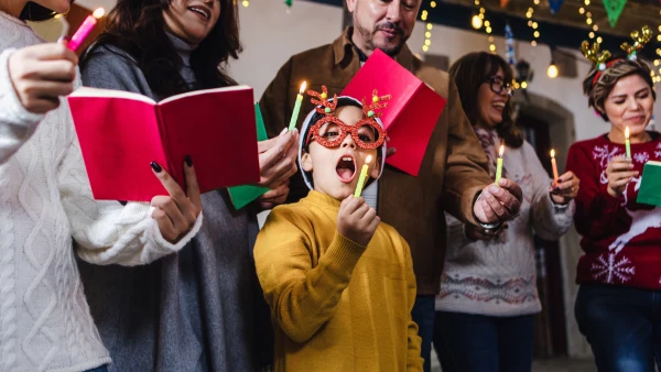 People singing and blowing out candles while wearing holiday sweaters.